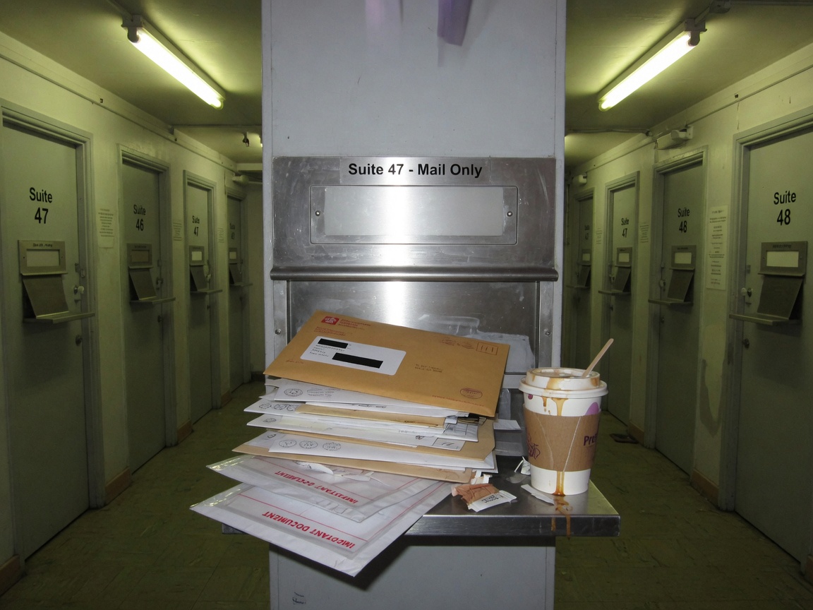 A virtual-office mail slot at night, unopened envelopes and a takeaway coffee on the ledge.